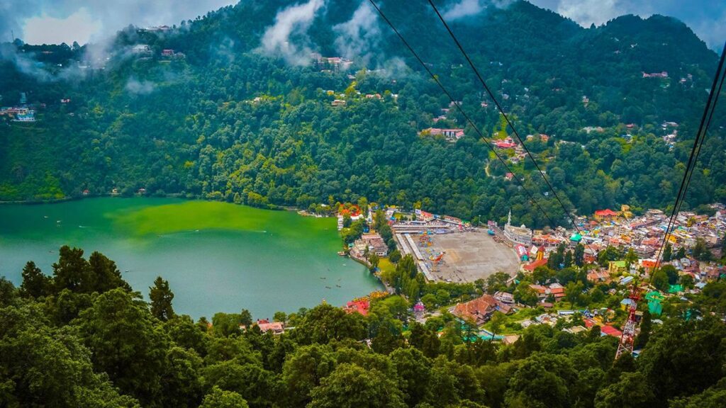 "Serene Naini Lake surrounded by lush green forests and misty floating clouds in Nainital – a perfect nature retreat."