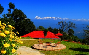 Scenic view of Kausani with snow-covered hills, lush gardens, trees, and dark blue sky.
