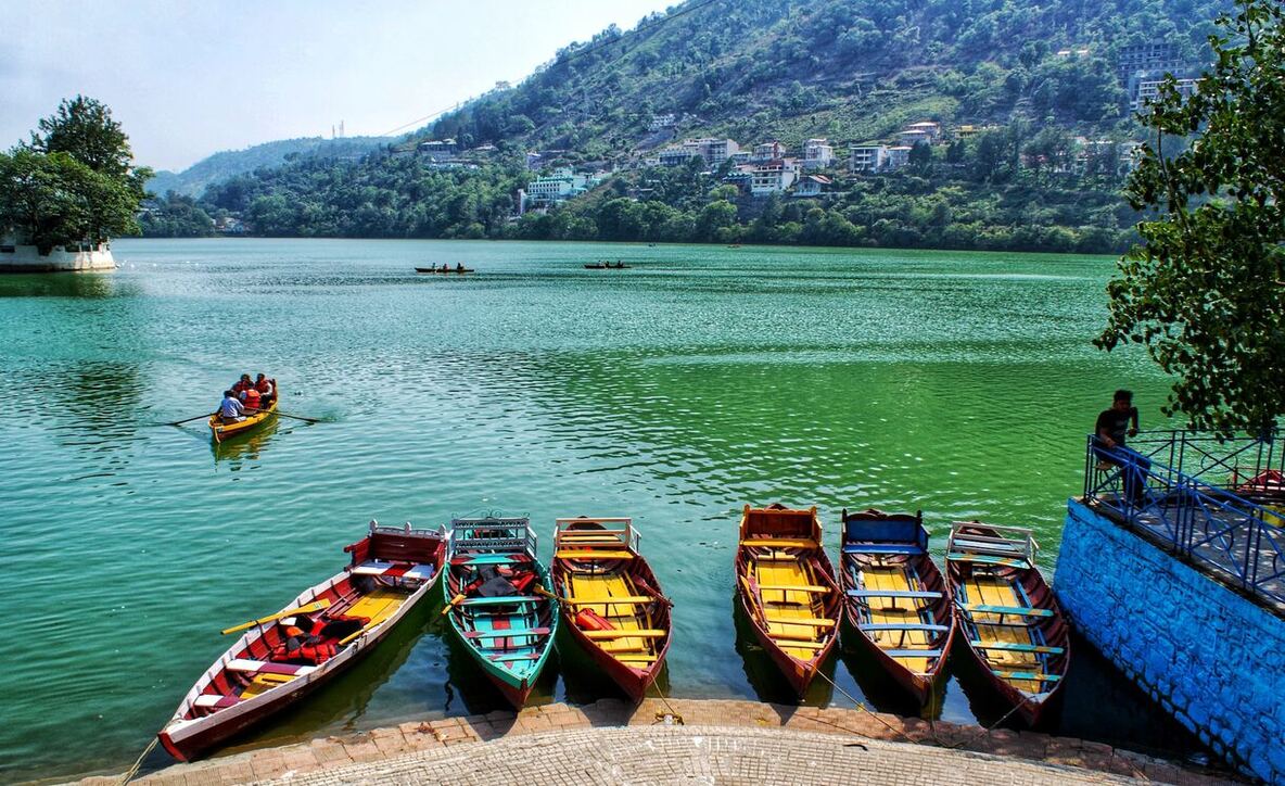 A serene blue lake surrounded by lush green hills, with colorful boats floating near the shore under a clear sky.