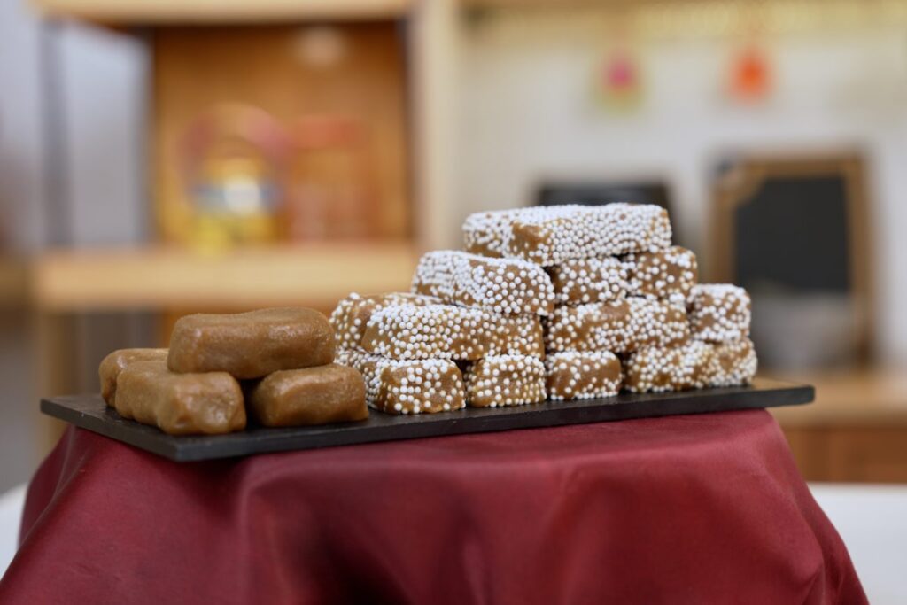 alt="Golden-brown Bal Mithai - Nainital's famous fudge-like sweet coated in sugar balls, displayed at a traditional Mall Road sweet shop"
