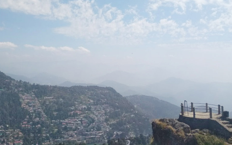 "Aerial view of Tiffin Top (Dorothy's Seat) in Nainital, showcasing lush green hills, panoramic Himalayan vistas, and a stone picnic perch."