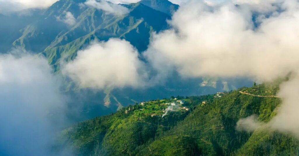 "Mussoorie in the rain with misty clouds drifting over lush green valleys β a serene monsoon landscape in the Himalayas."