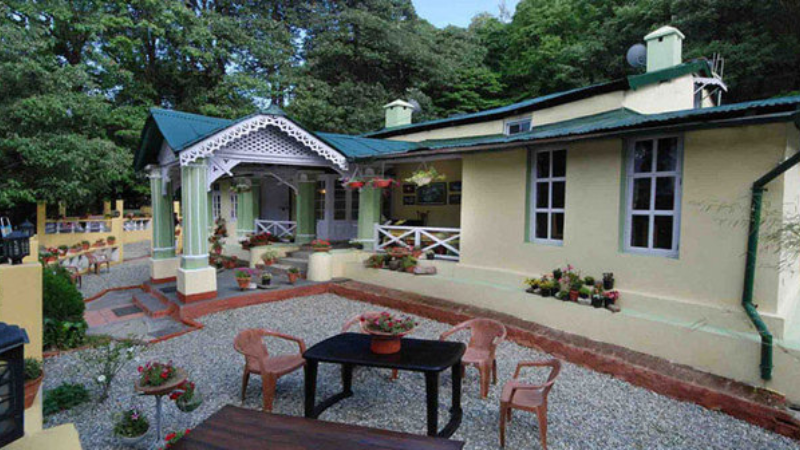A charming wooden cottage-style homestay surrounded by pine trees in Ayarpatta Hills, Nainital. The cozy balcony offers panoramic views of the misty hills, with traditional architecture and a warm, inviting ambiance.