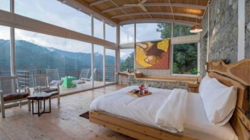"A warm and inviting bedroom at Khursheed Villa, featuring wooden furnishings, soft lighting, and plush bedding, with large windows offering glimpses of the surrounding forest."