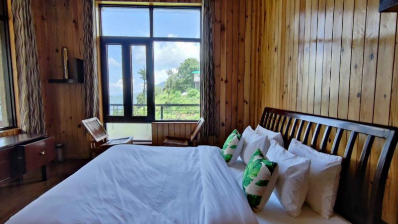 "A tranquil balcony view from Valley View Homestay, overlooking a lush fruit orchard and terraced hillsides, with a golden sunset painting the sky in warm hues over the distant mountains."